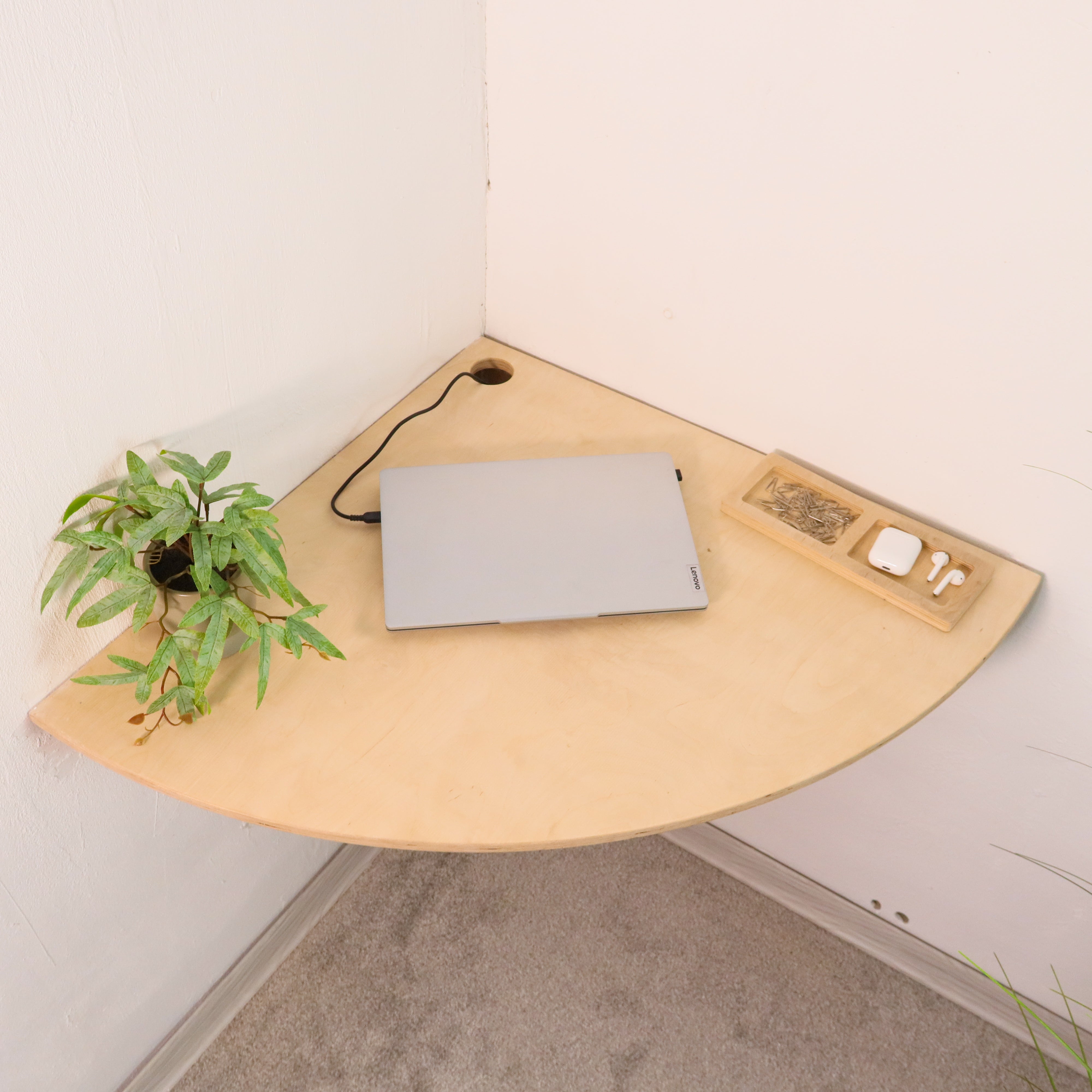 Wooden corner desk with a laptop, plant, and small table on a light-colored floor.